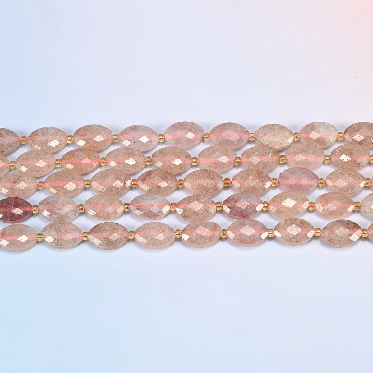 Several strands of strawberry quartz faceted flat oval beads laid in straight rows with gold seed bead spacers