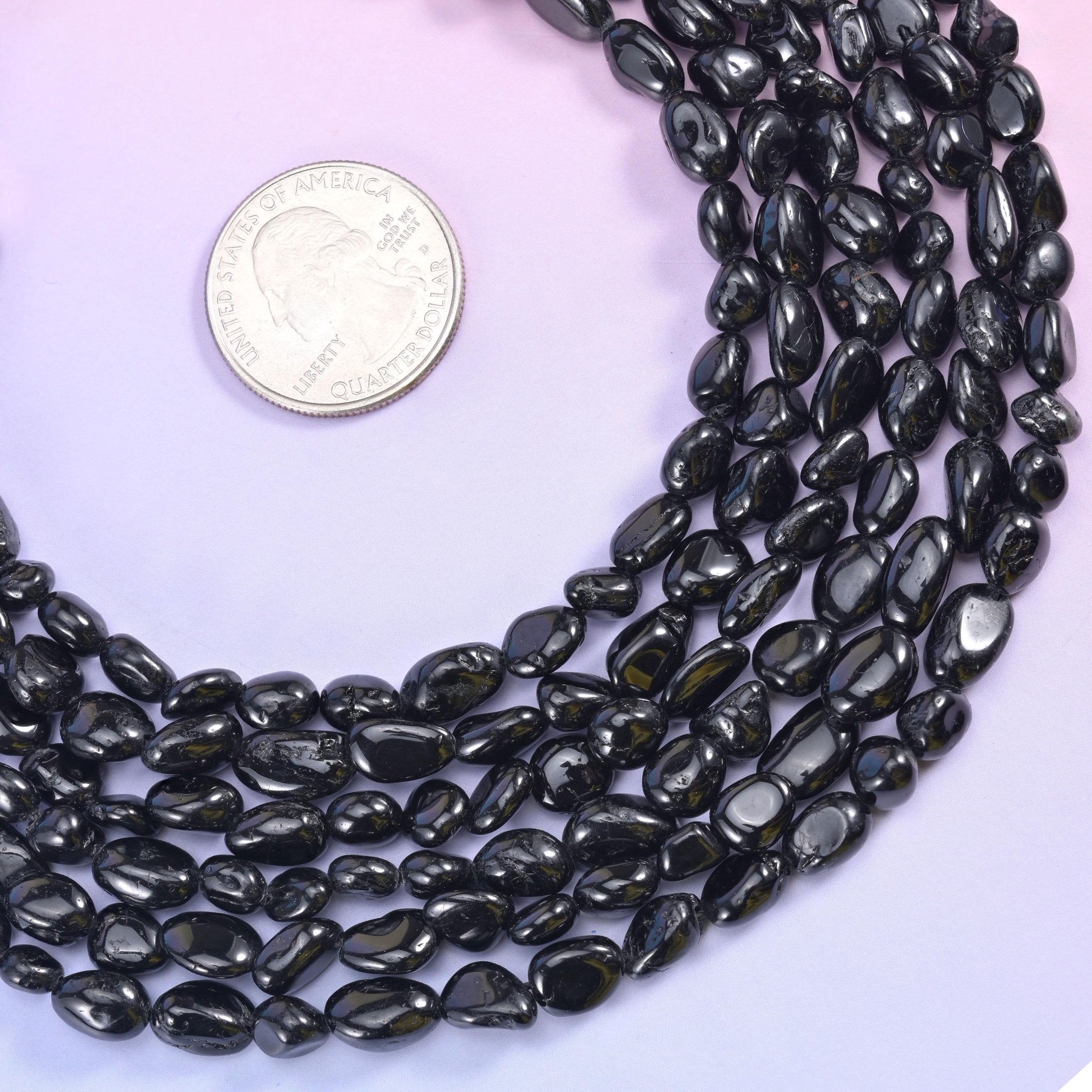 Black tourmaline strand coiled beside a silver coin, showing the 6-8mm bead range