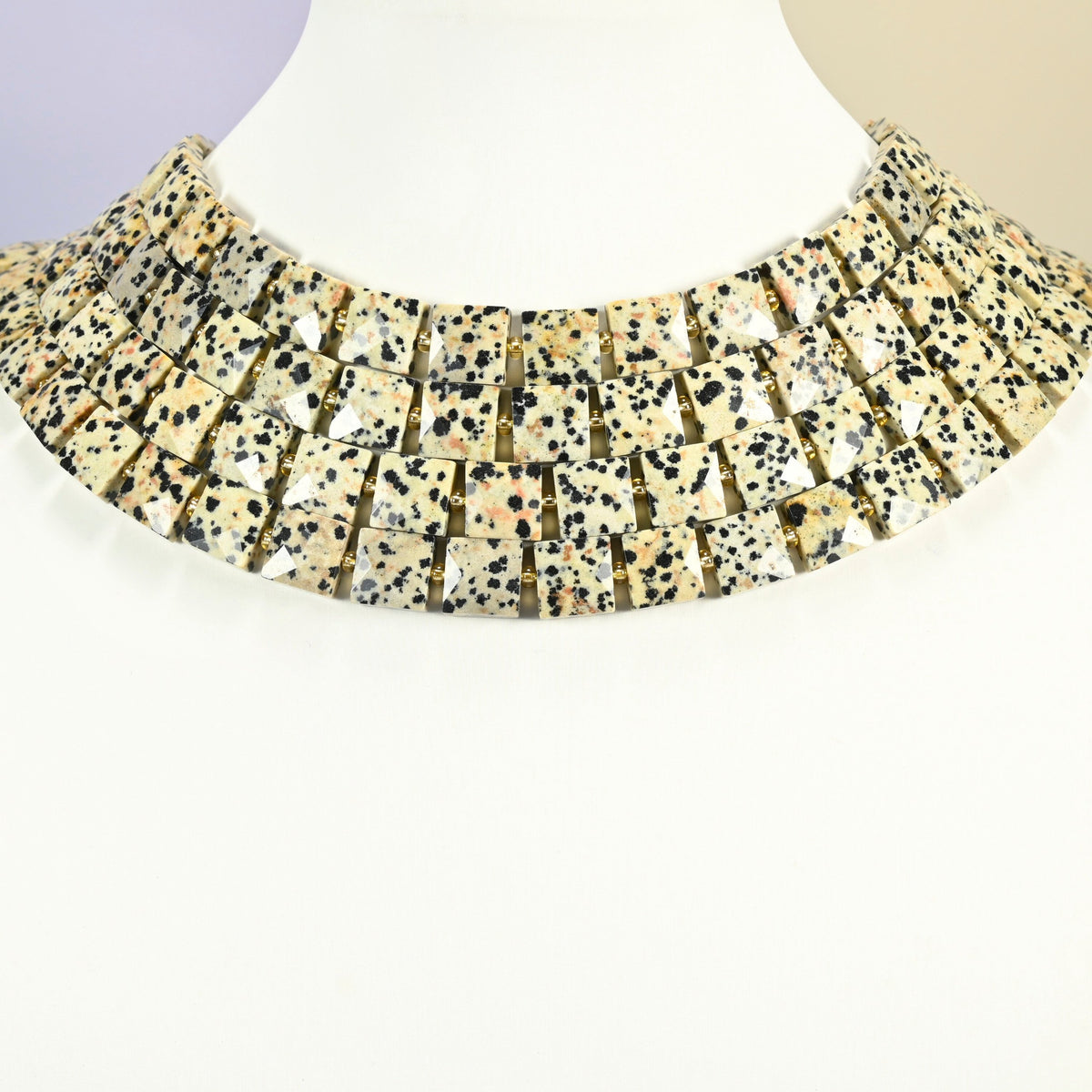 Dalmatian jasper faceted flat square strands arranged as a layered collar on a white display bust, spotted cream beads across the neck