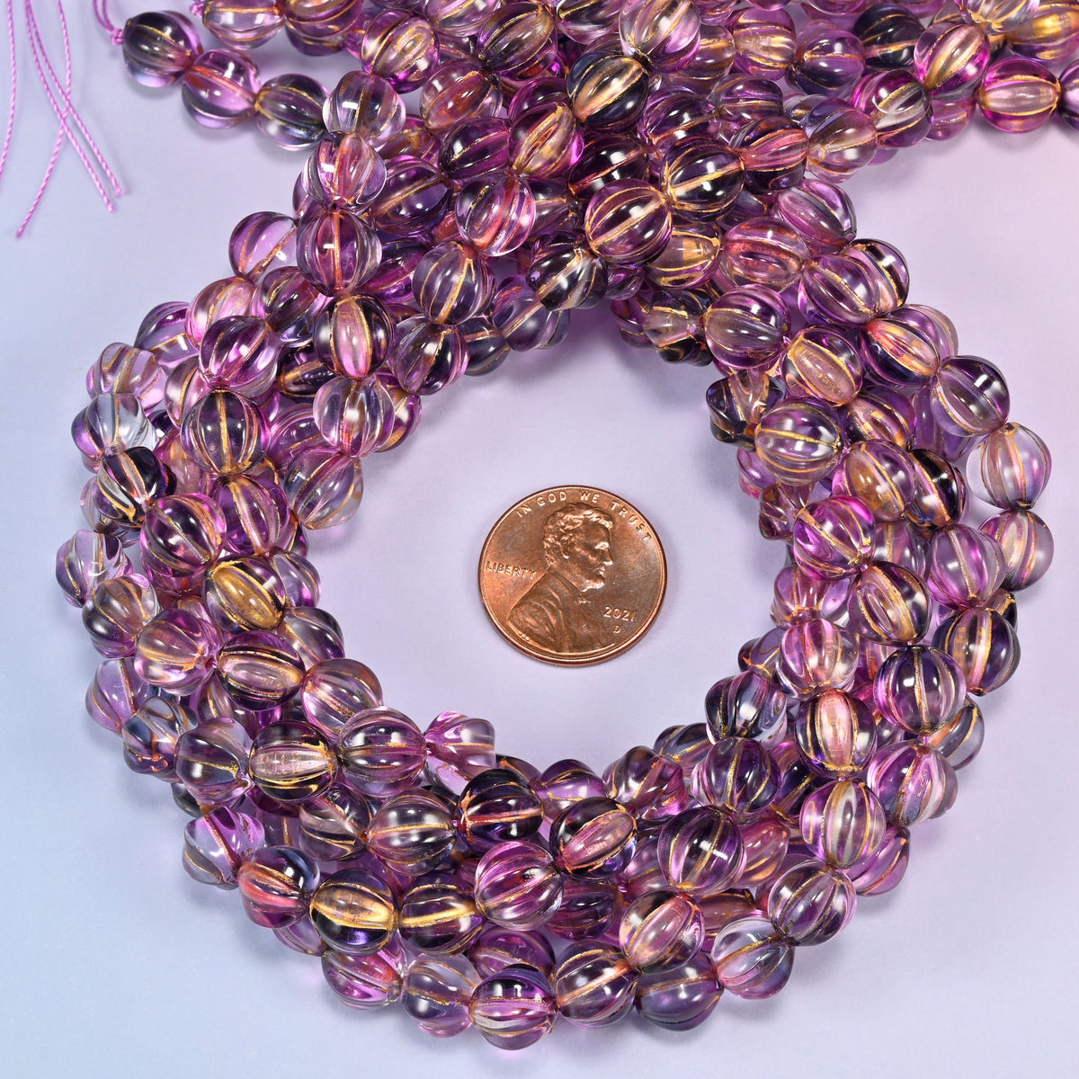 Pink blue gold pumpkin glass beads coiled into a tight spiral, the strand end trailing off the top corner.