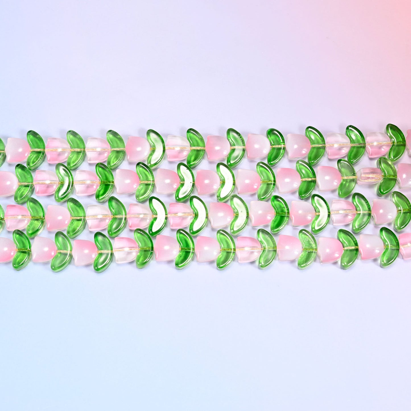 Close-up macro view of pink tulip and green leaf glass beads in a dense repeating row pattern on a lavender and pink gradient background.
