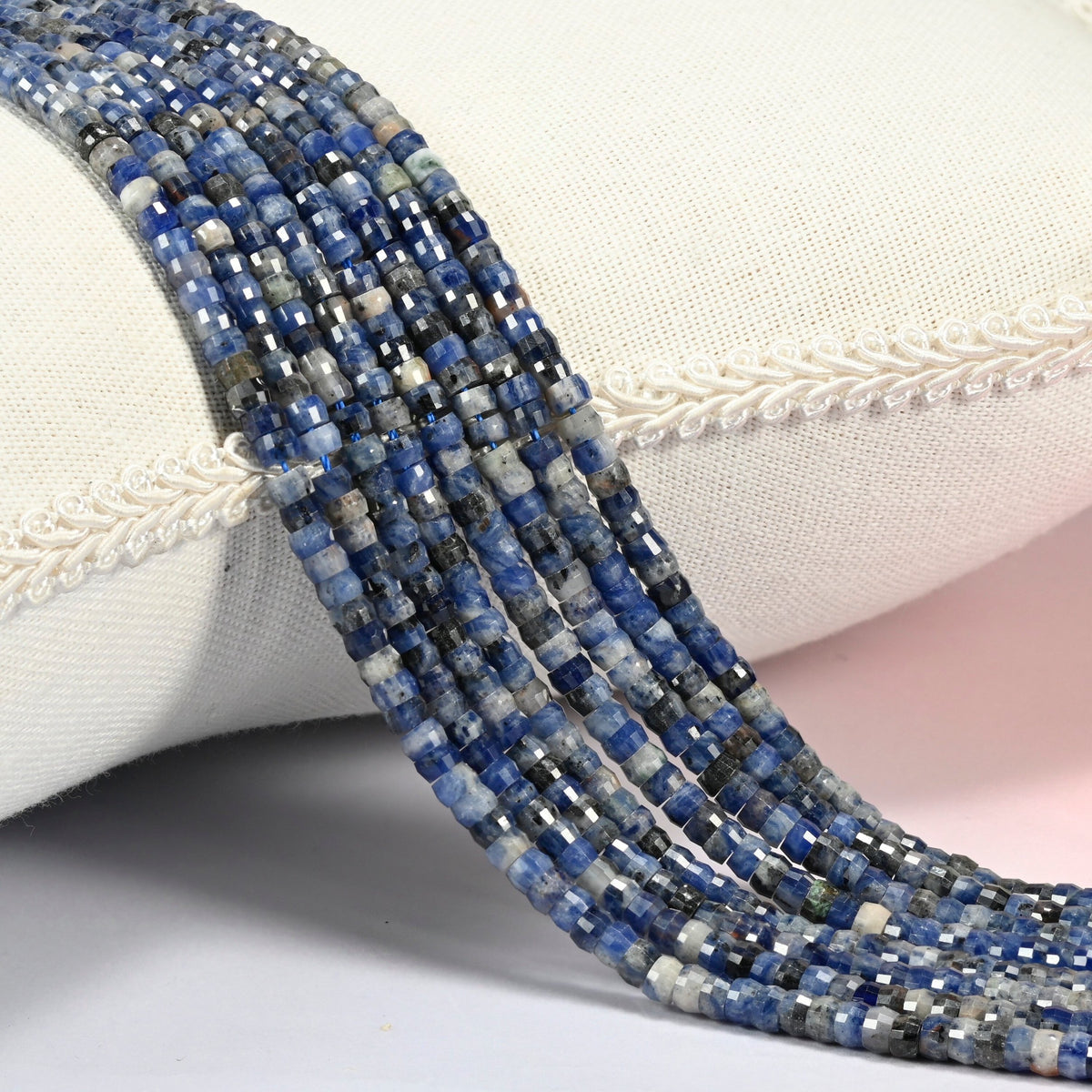 Sodalite faceted heishi disc beads 2x4mm, several strands draped over a white cushion