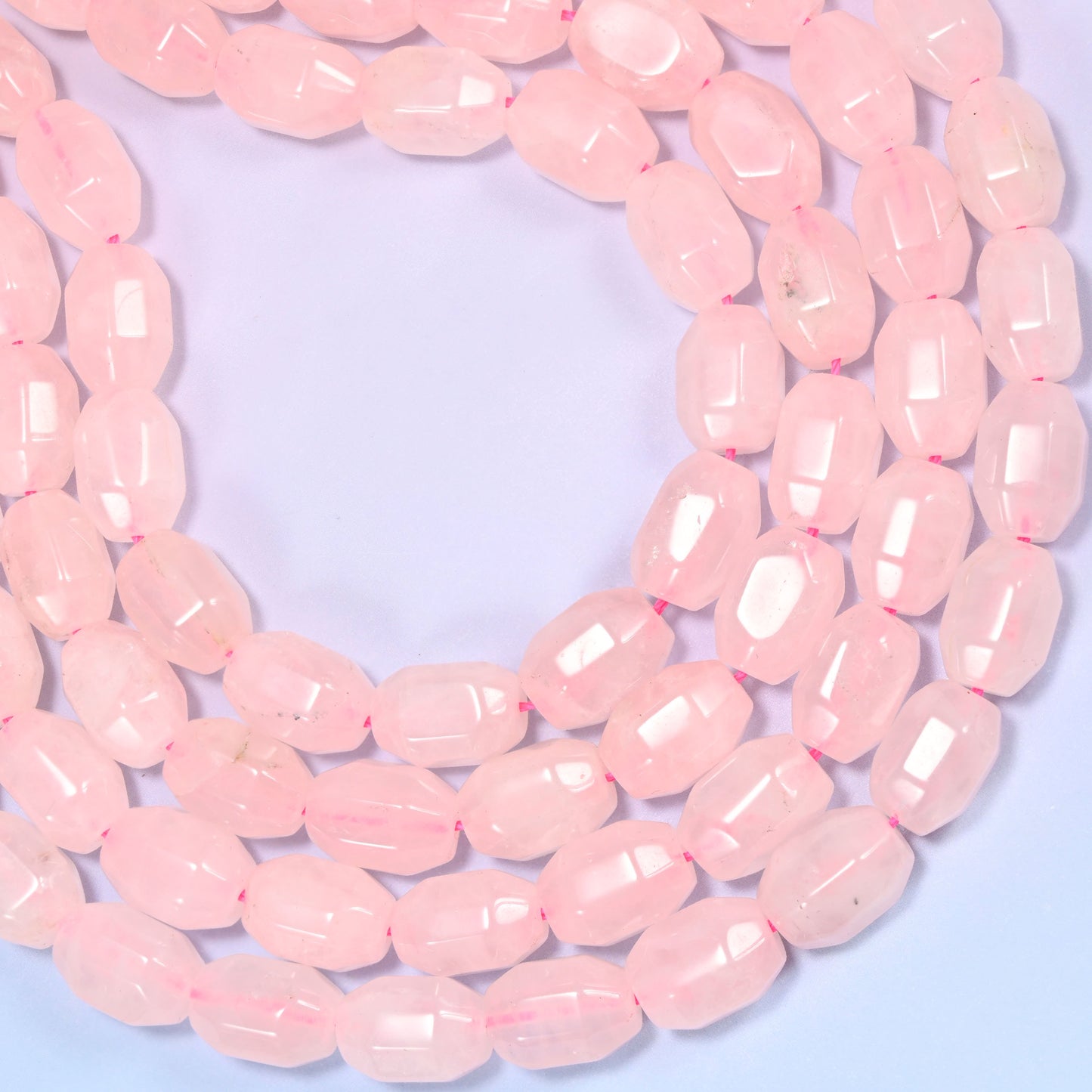 Wide circular coil of Rose Quartz faceted barrel bead strands forming a full wreath shape on a light lavender background.