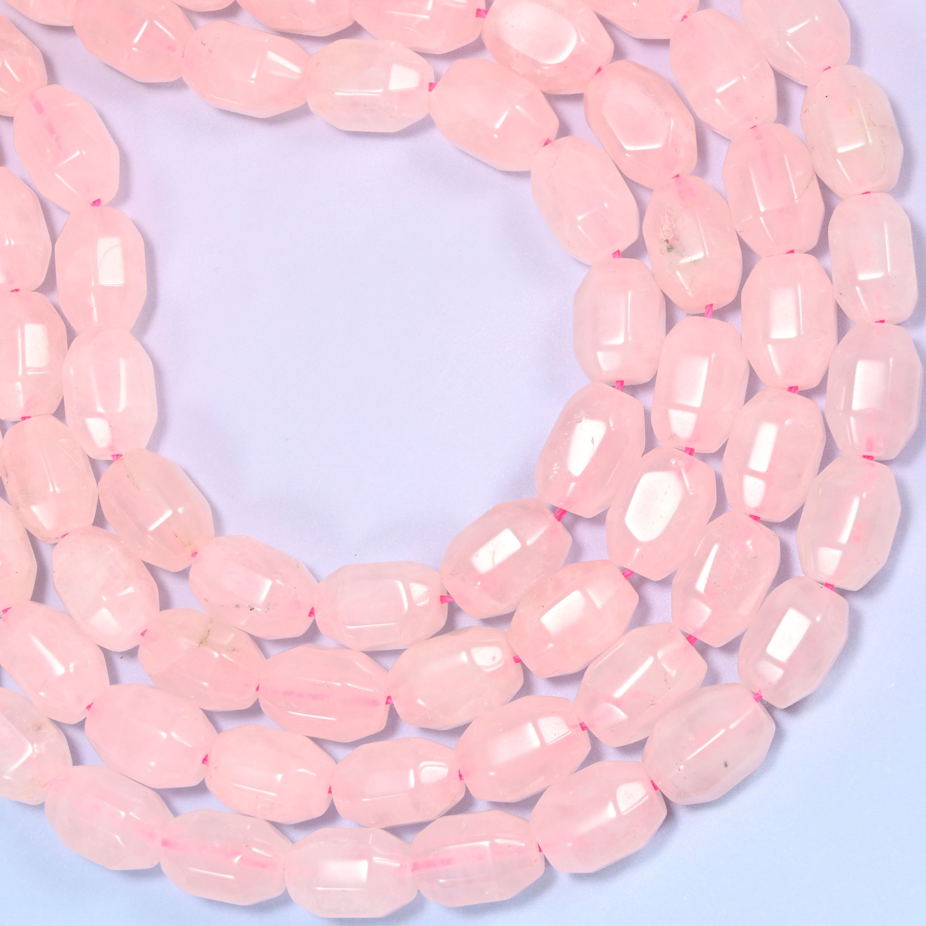 Wide circular coil of Rose Quartz faceted barrel bead strands forming a full wreath shape on a light lavender background.