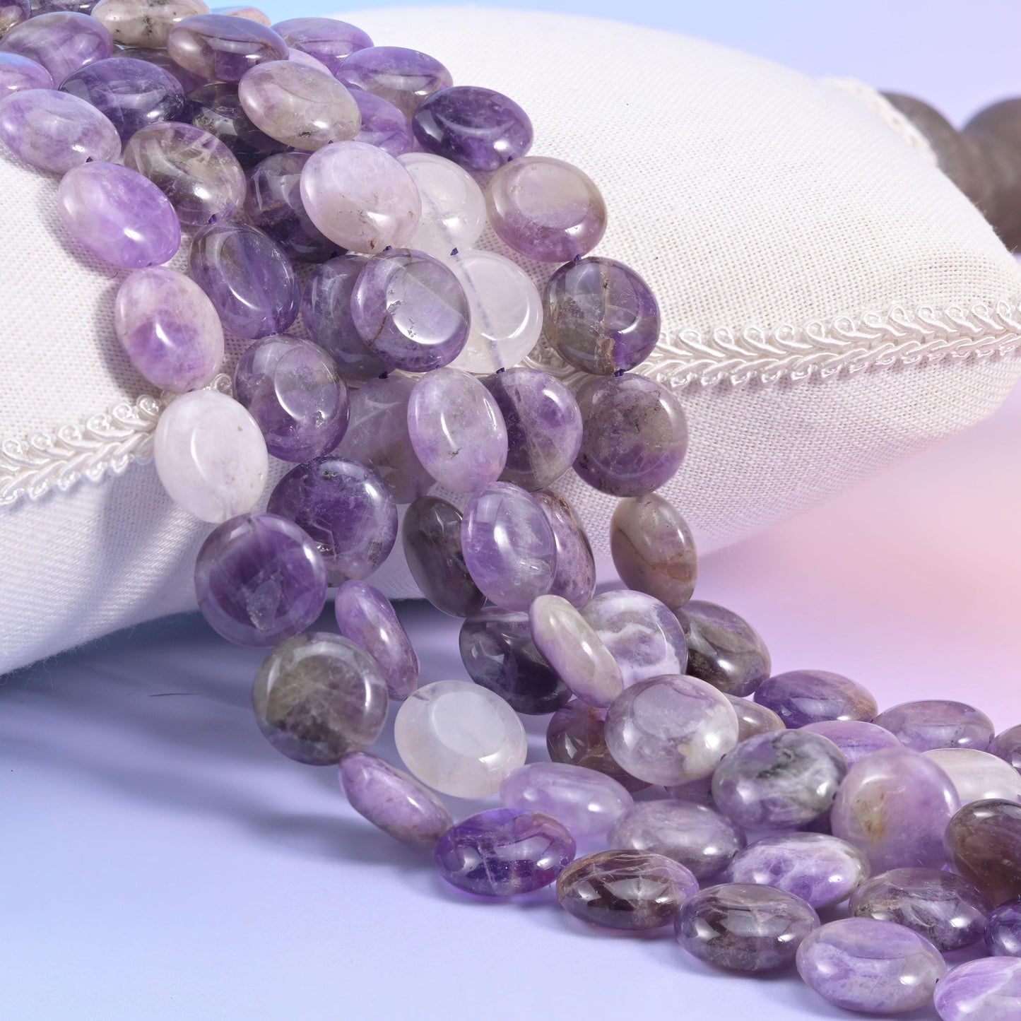 Amethyst coin bead strands resting against a white cushion in pale violet