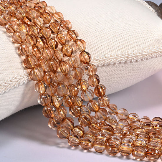 Brown pumpkin glass beads, 8mm fluted melon rounds, several strands draped over a white cushion.