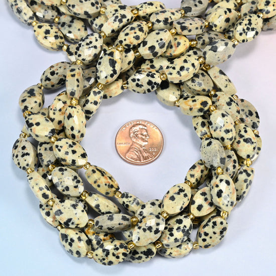 Dalmatian jasper faceted flat oval beads 9x14mm coiled in a loop around a US penny for scale, close-up of the faceted flat oval shape