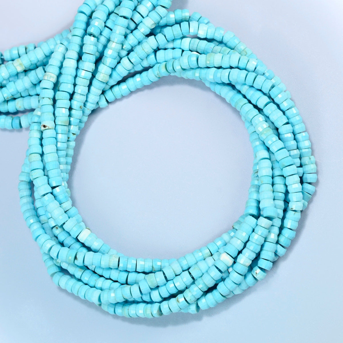 Dyed blue howlite faceted heishi disc beads coiled into overlapping loops, whole strands of bright turquoise stone