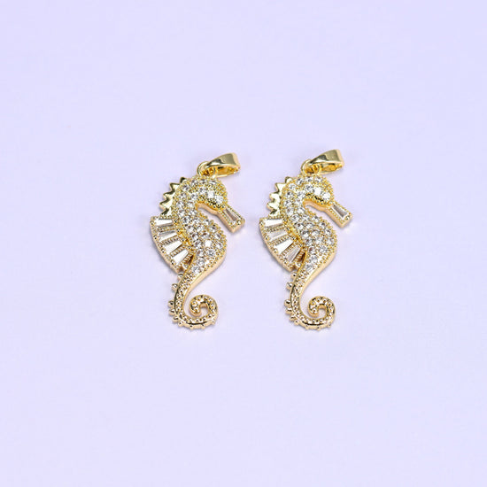 Two 18K gold plated sea horse zirconia charms side by side, each body paved in round and baguette clear stones with a curled tail.