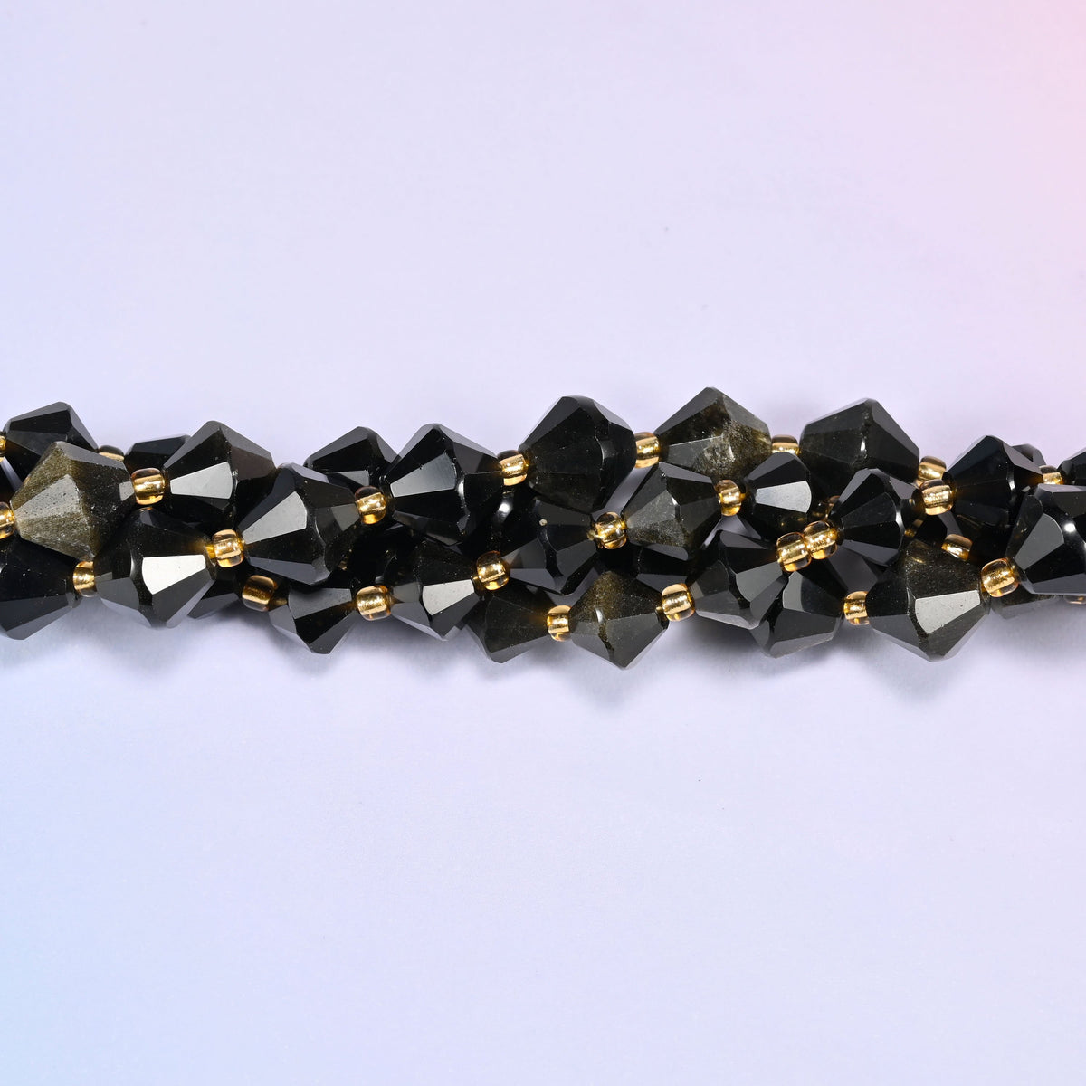 Gold obsidian bicone beads shown as a single strand laid straight across, near-black beads beside ones lit right through with gold.