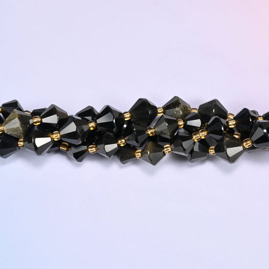 Gold obsidian bicone beads shown as a single strand laid straight across, near-black beads beside ones lit right through with gold.
