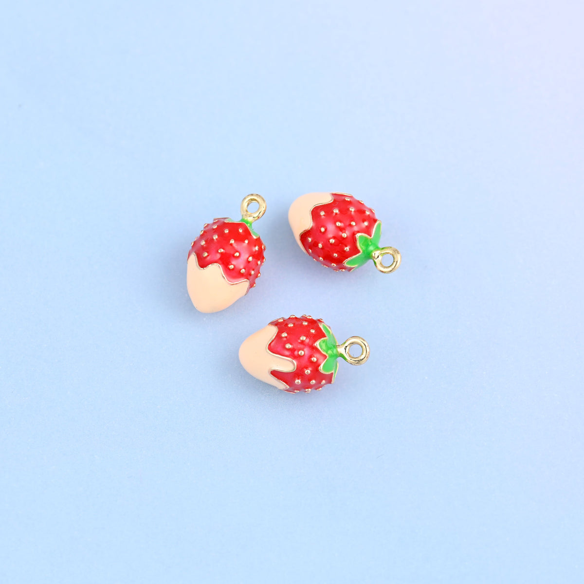 Three strawberry charms dipped in light orange enamel, green leaf and small gold ring at the top.