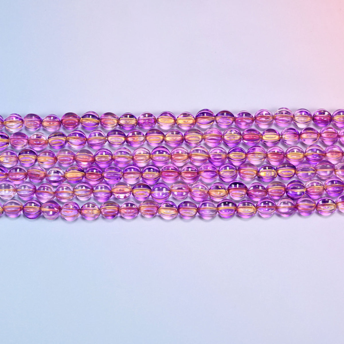 Close-up of 8mm purple gold pumpkin glass beads in four horizontal rows, showing the carved melon ribs.