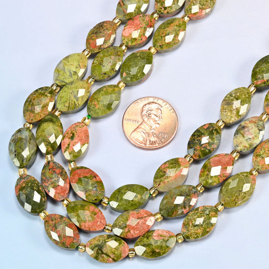 Close view of unakite faceted flat oval strands curving beside a US penny for scale