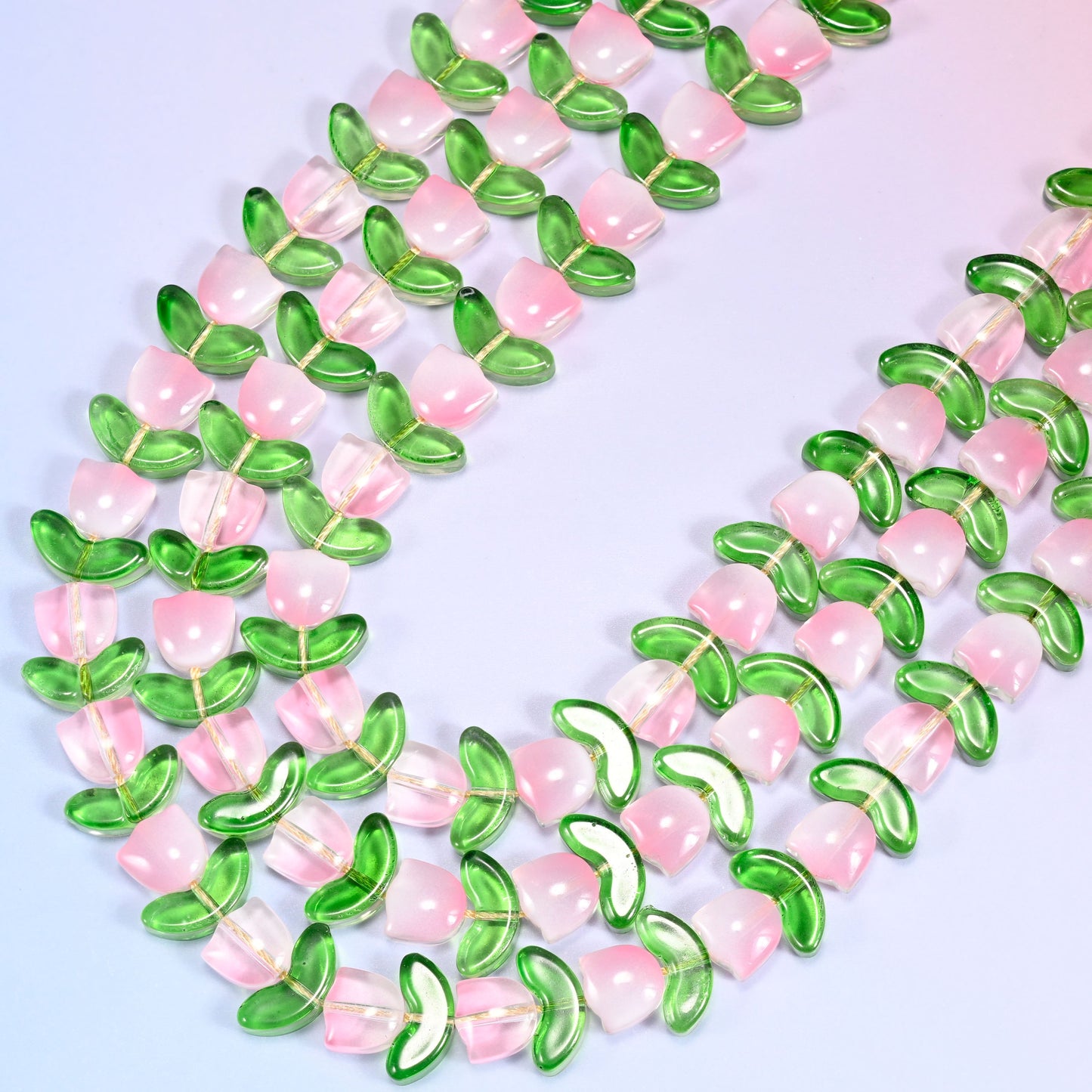 Circular coil of pink tulip and green leaf glass bead strands forming a wreath shape on a lavender background.