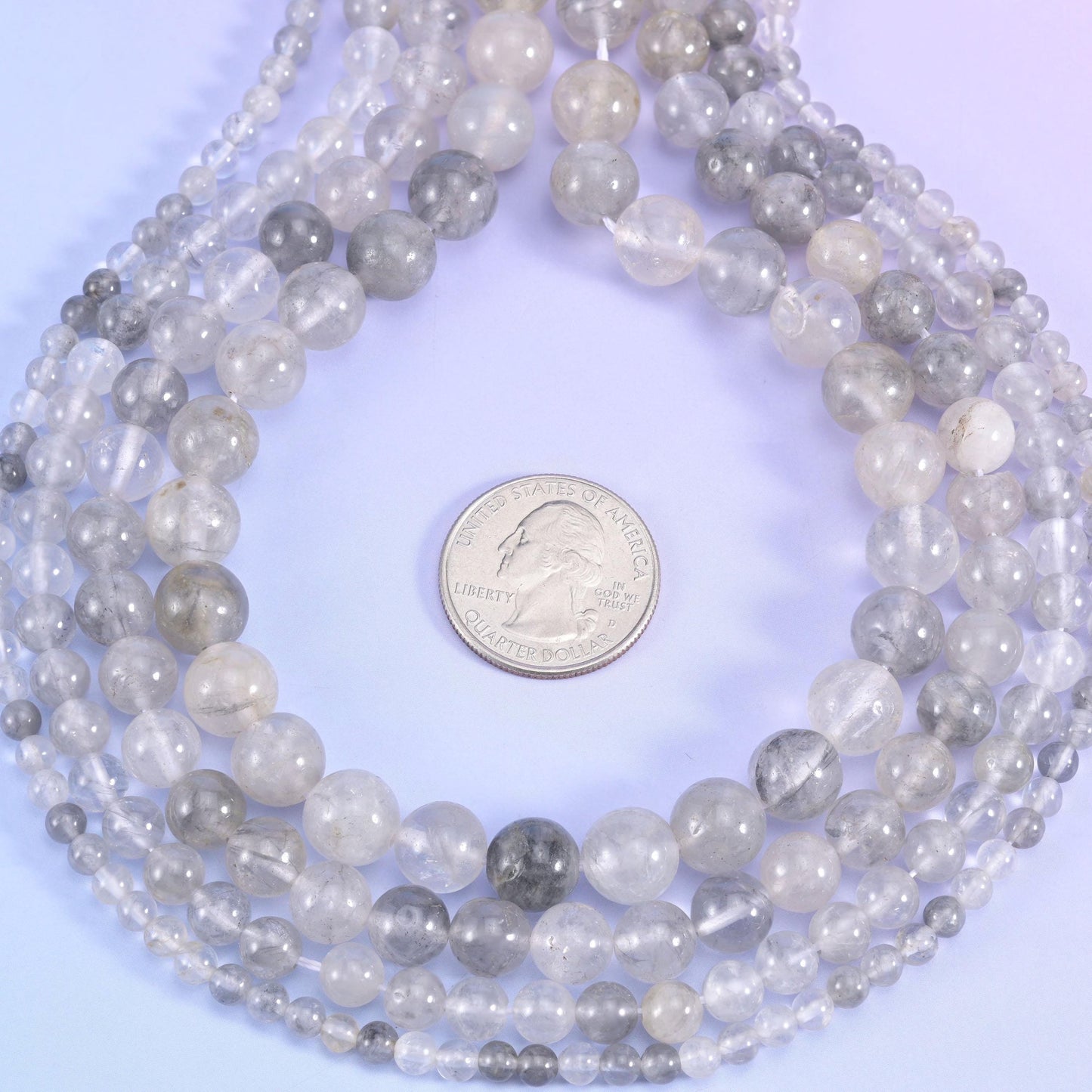Translucent quartz drifting from near-clear to soft dove grey, with milky white veils and smoky patches trapped inside, polished to a glossy round with no facets at all.
