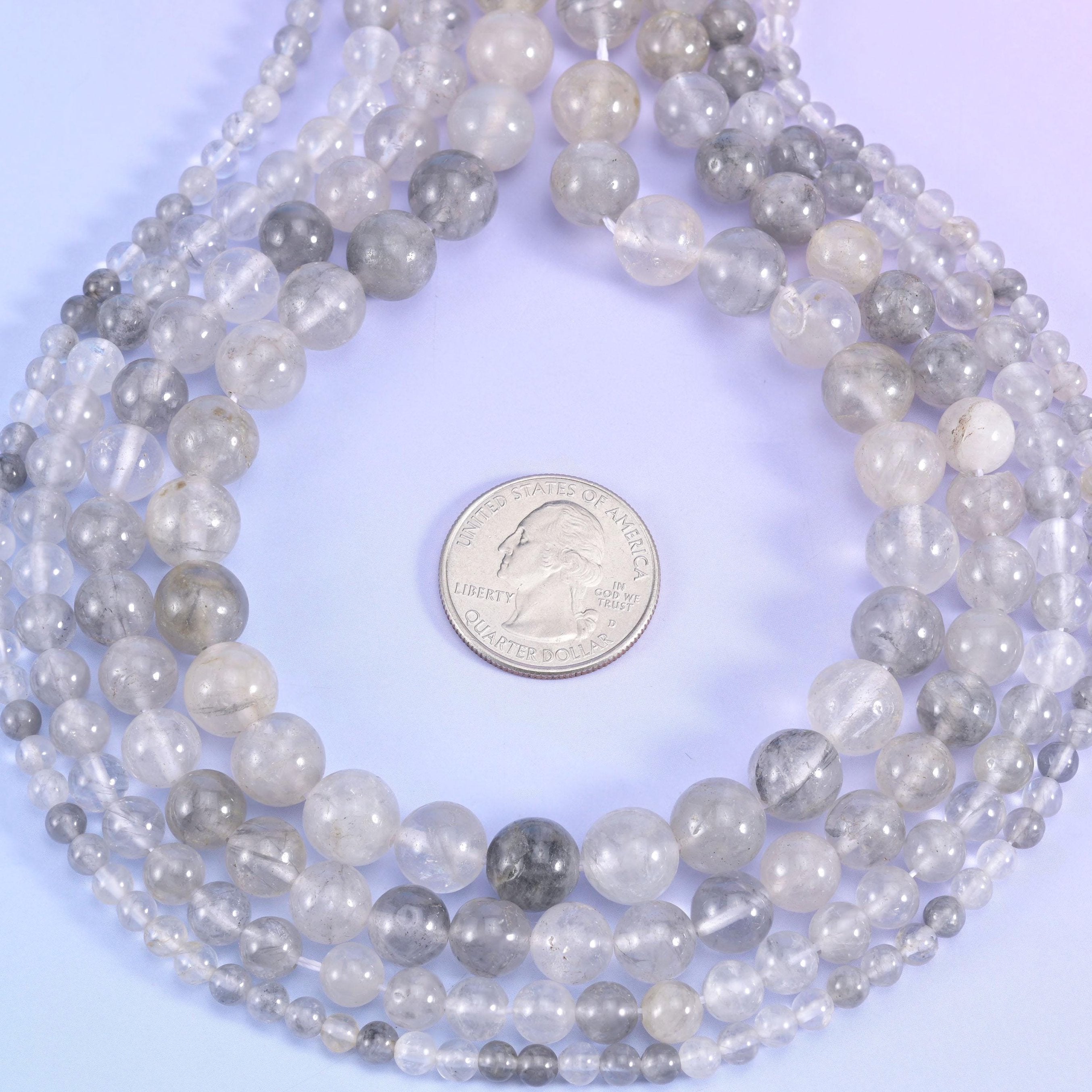 Translucent quartz drifting from near-clear to soft dove grey, with milky white veils and smoky patches trapped inside, polished to a glossy round with no facets at all.
