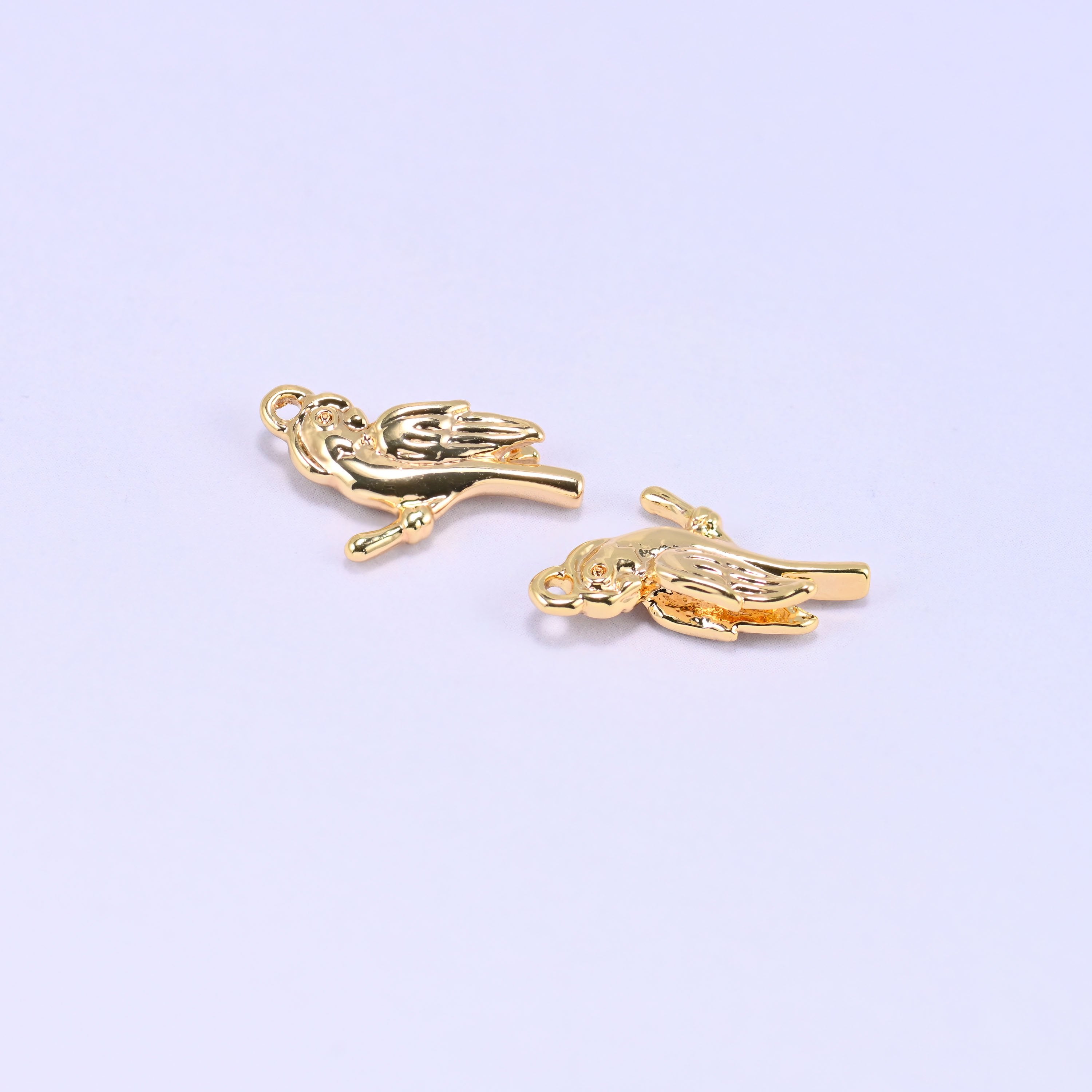 Small gold charms bird, two 18K gold plated brass charms close up on a lilac backdrop