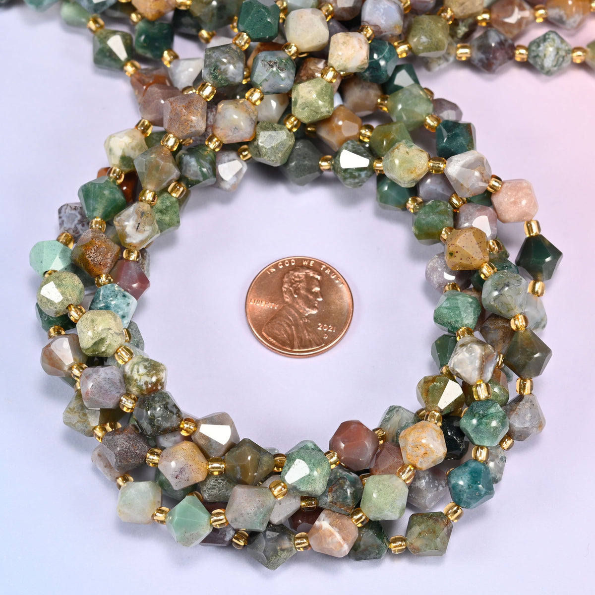 Indian Agate faceted bicone beads 8mm with gold-tone spacers, strand coiled with a penny centered, close-up of the beads