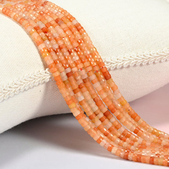 Red aventurine faceted heishi disc beads 2x4mm, several strands draped over a white cushion