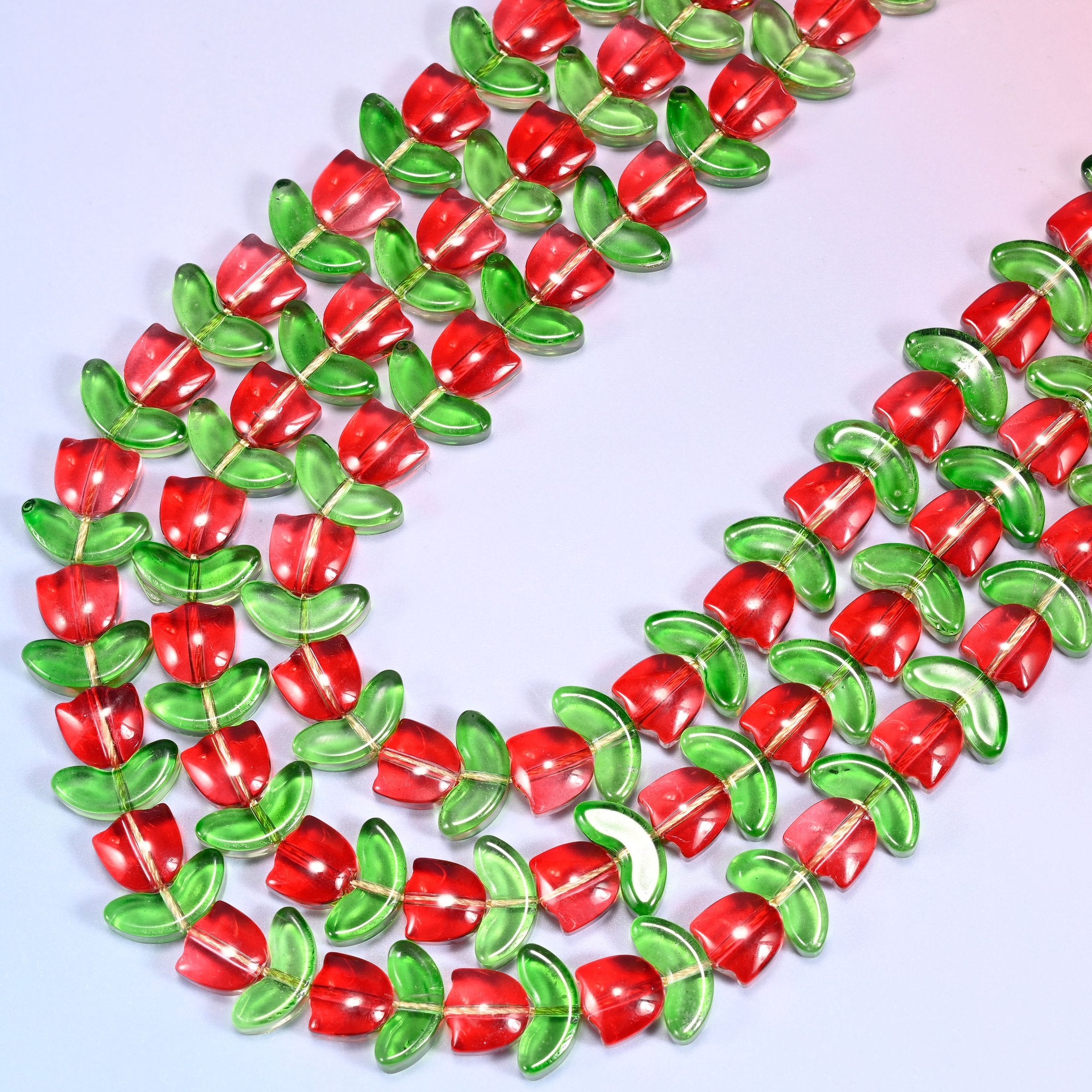 Circular coil of red tulip and green leaf glass bead strands forming a wreath shape on a lavender background.