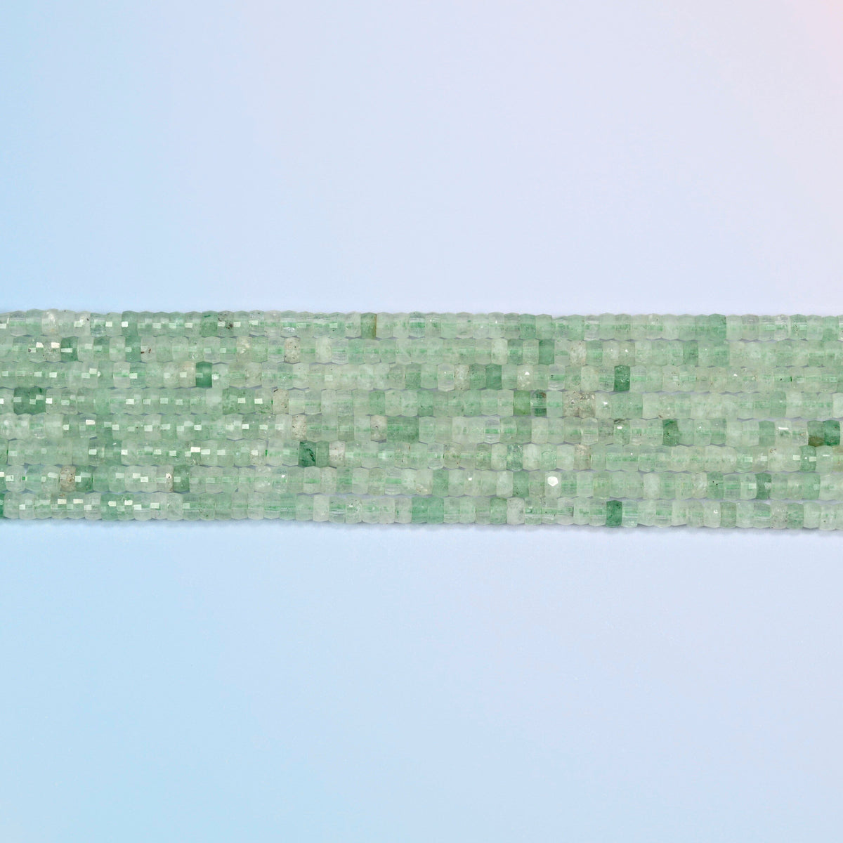 Several strands of green strawberry quartz faceted heishi disc beads laid in straight rows