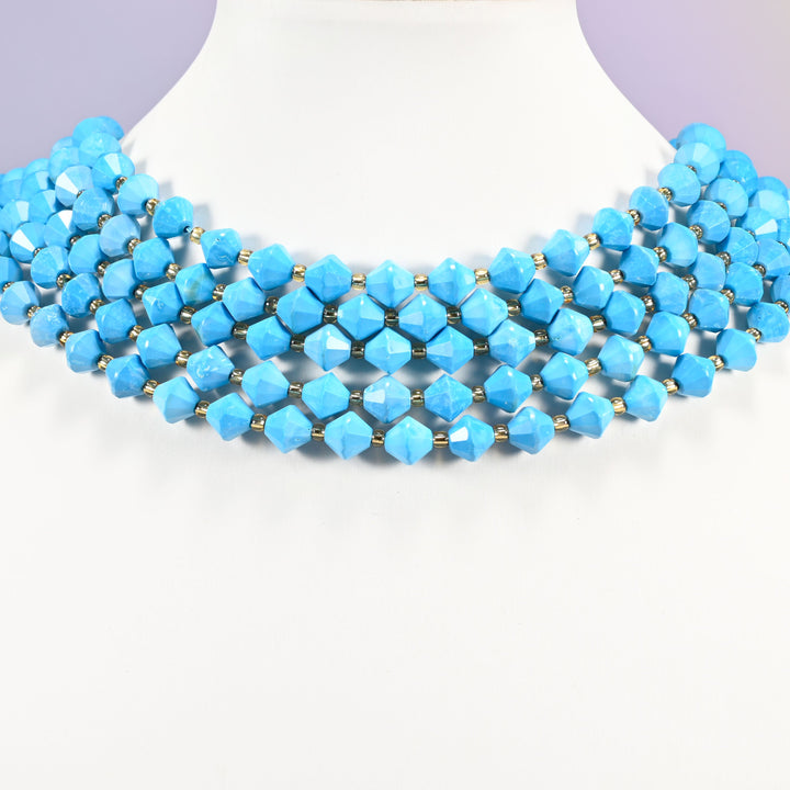 Dyed blue howlite faceted bicone beads on a white neck display, four strands around the base of the bust.