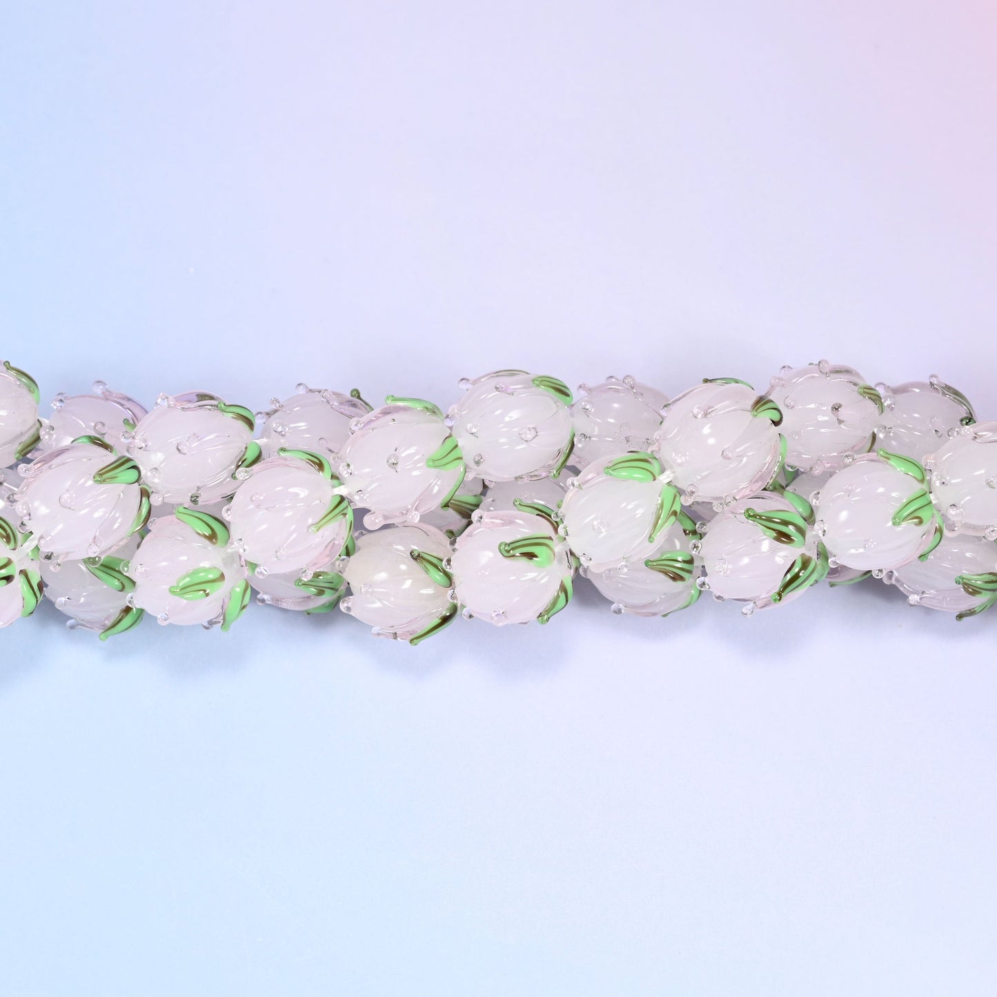 Light pink tulip bud-shaped lampwork glass beads, hand-formed with sculpted petal detailing that gives a realistic flower bud look, accented with a green leaf detail at the base.