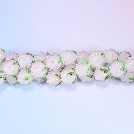 Light pink tulip bud-shaped lampwork glass beads, hand-formed with sculpted petal detailing that gives a realistic flower bud look, accented with a green leaf detail at the base.