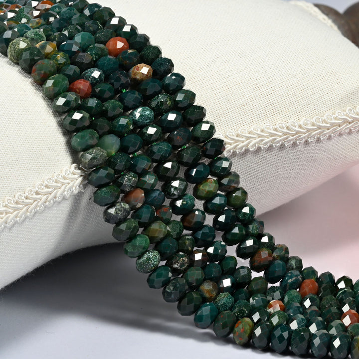 Oriental jasper faceted rondelle beads 5x8mm in deep forest green with brick red accents, several strands draped over a white cushion
