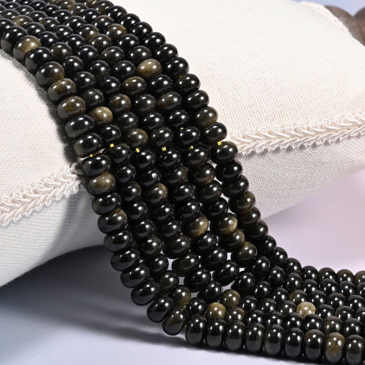 Close-up of multiple strands of polished Gold Obsidian rondelle beads with a golden sheen, draped over a cream fabric jewelry display bust.
