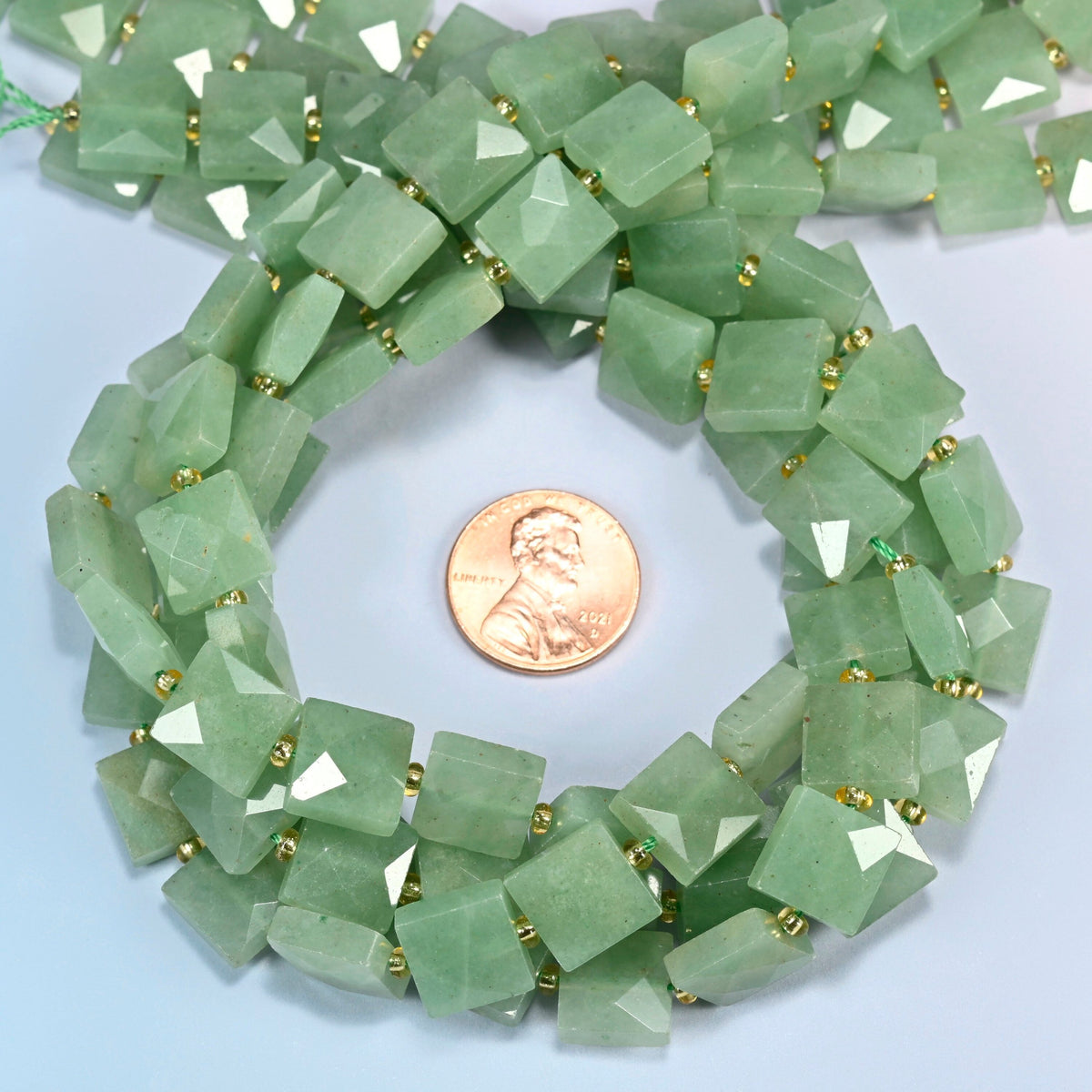 Natural green aventurine faceted flat square beads 10x10mm coiled in a loop around a US penny for scale, close-up of the faceted flat square shape