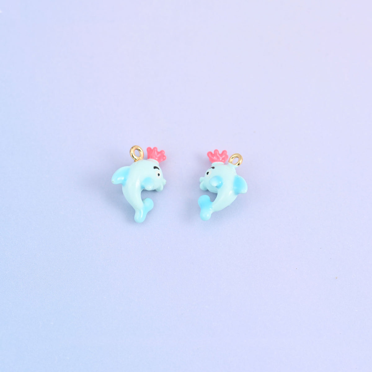 Two light blue dolphin charms with crowns, front and back, each crown moulded in pink.