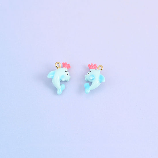 Two light blue dolphin charms with crowns, front and back, each crown moulded in pink.