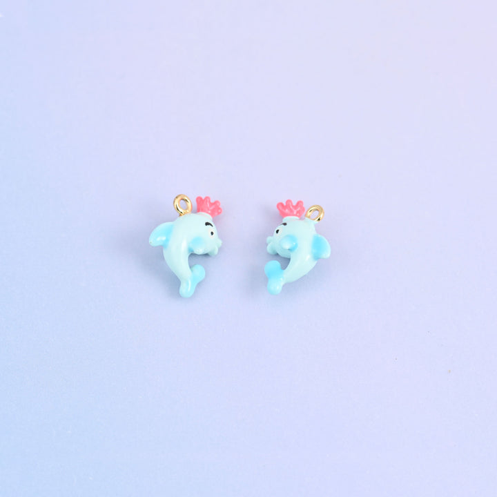 Two light blue dolphin charms with crowns, front and back, each crown moulded in pink.