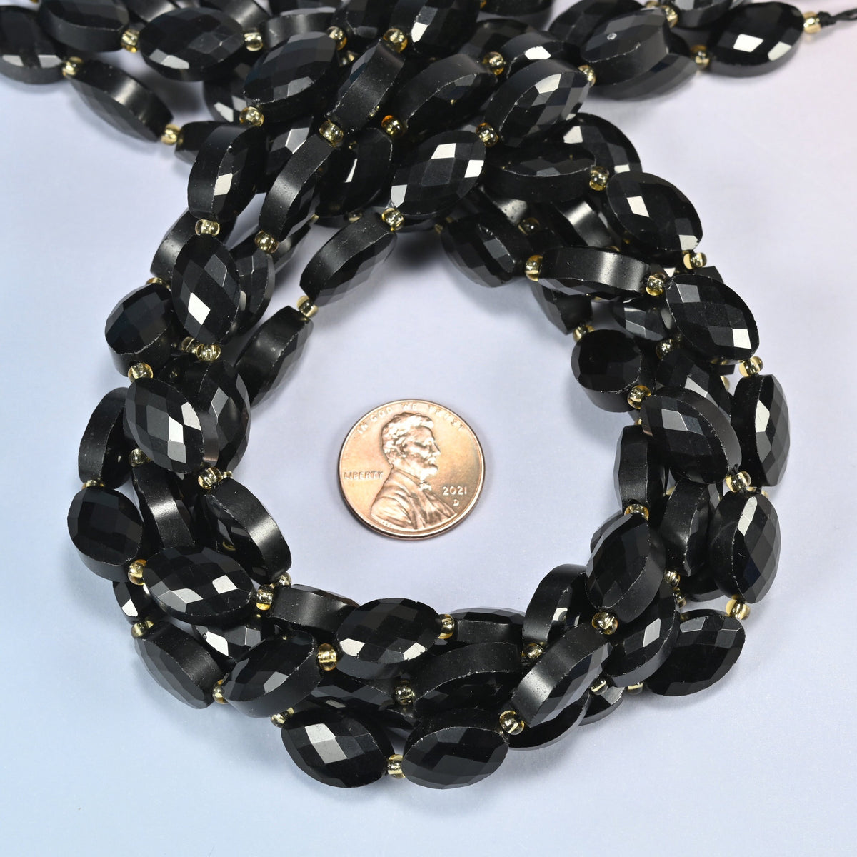 Black onyx faceted flat oval beads 9x14mm coiled in a loop around a US penny for scale, close-up of the faceted flat oval shape