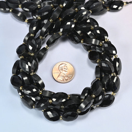 Black onyx faceted flat oval beads 9x14mm coiled in a loop around a US penny for scale, close-up of the faceted flat oval shape
