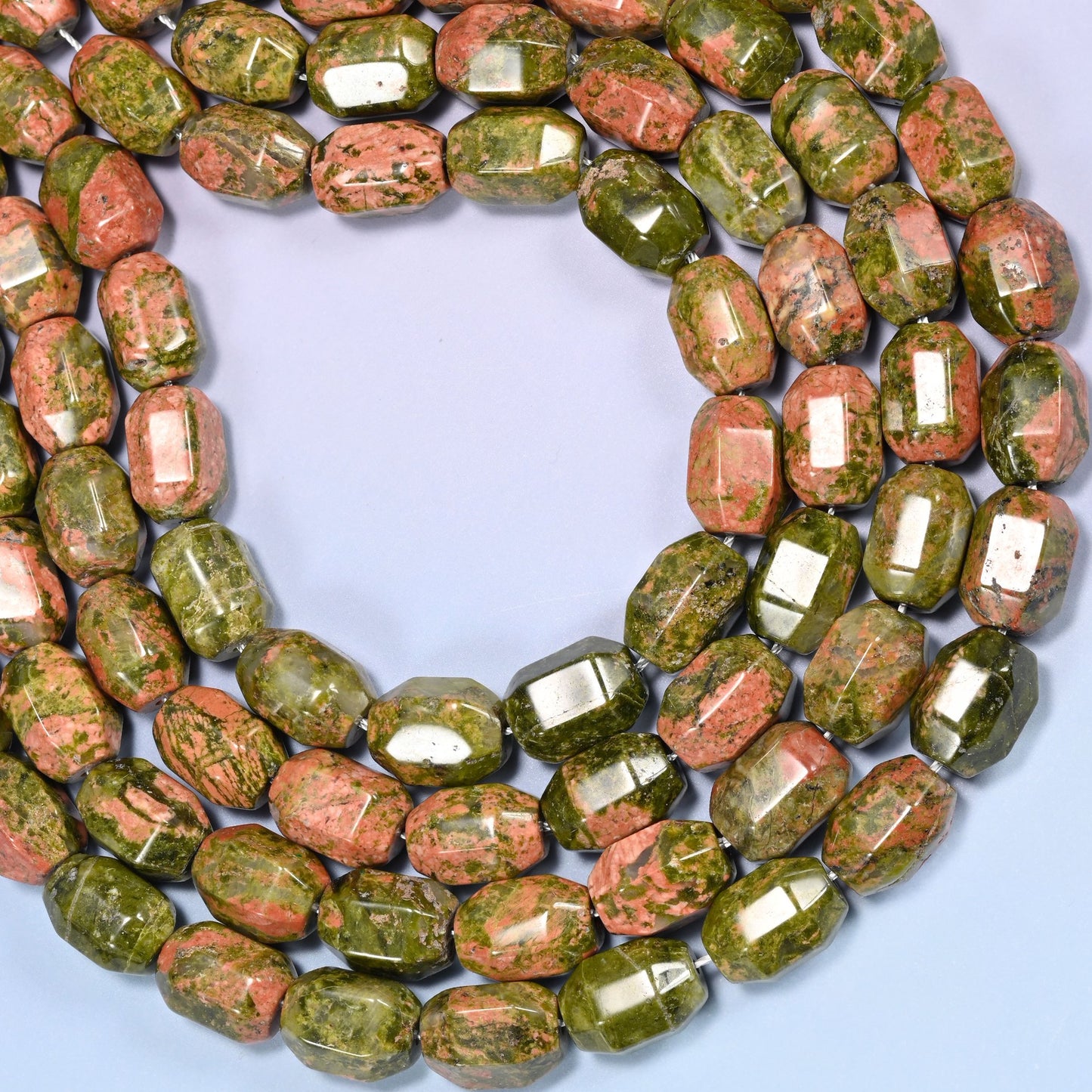 Close-up of a circular coil of faceted Unakite barrel beads on a light blue background.