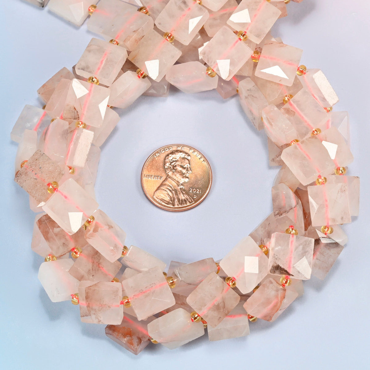 Natural red hematoid quartz faceted flat square beads 10x10mm coiled in a loop around a US penny for scale, close-up of the faceted flat square shape