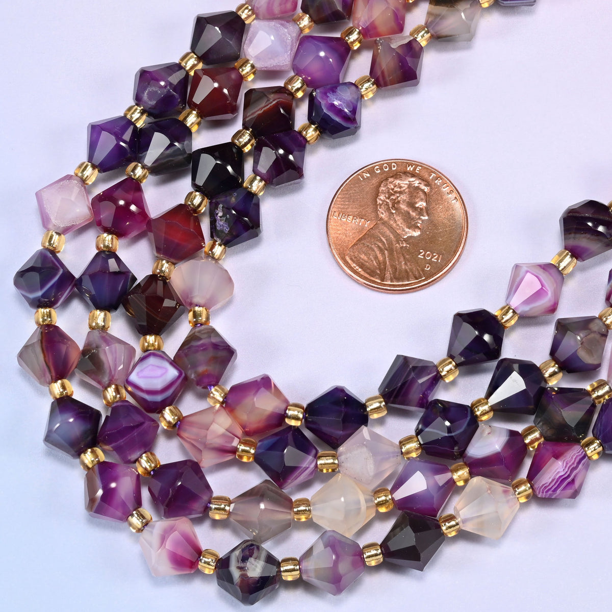 Close-up of 8mm Dyed Purple Strip Agate faceted bicone beads coiled into a circle, showing the purple color and natural banded striping in the stone.