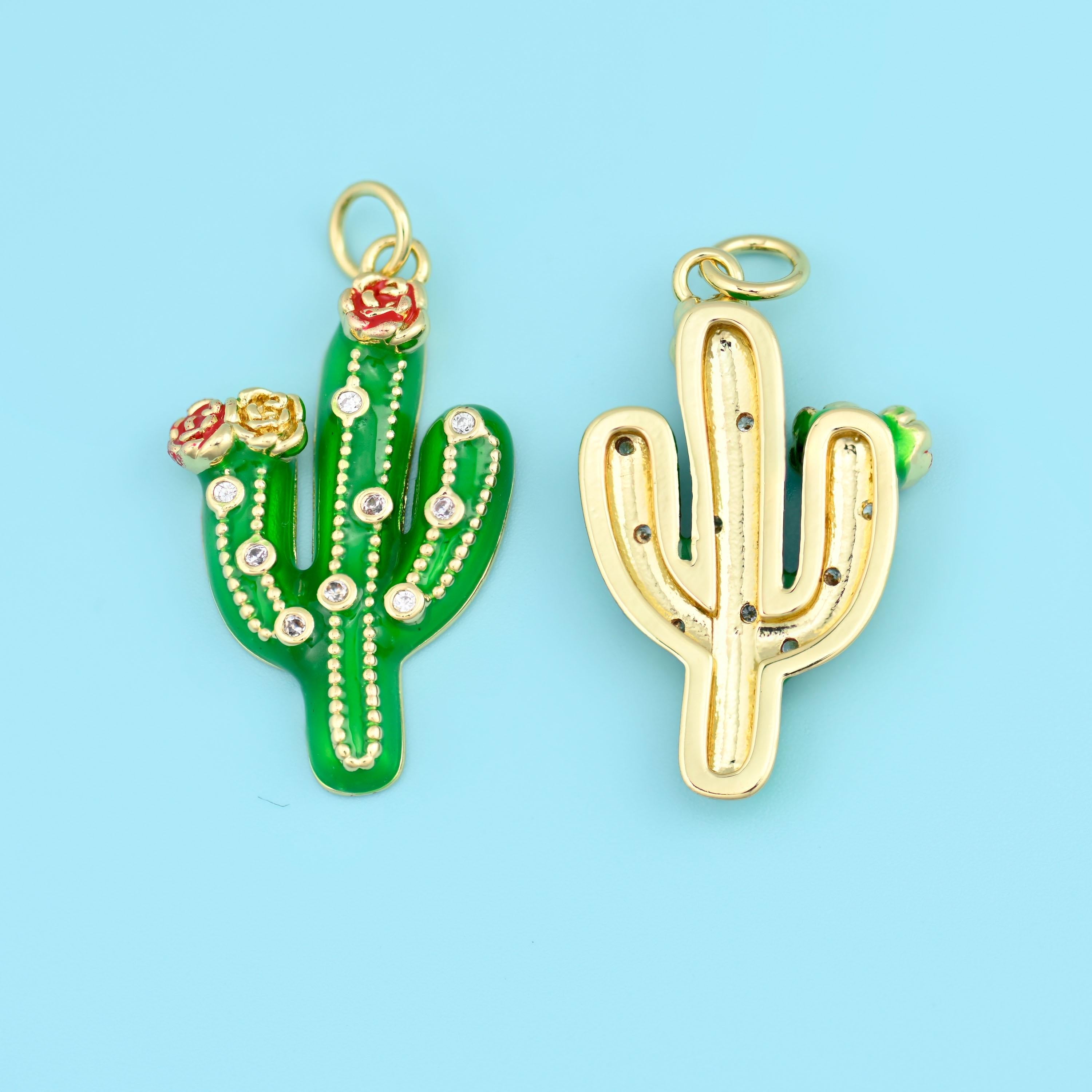 A three-armed saguaro in glossy enamel with a tiny coral red bloom at the crown, ribbed down the body with dotted lines of…