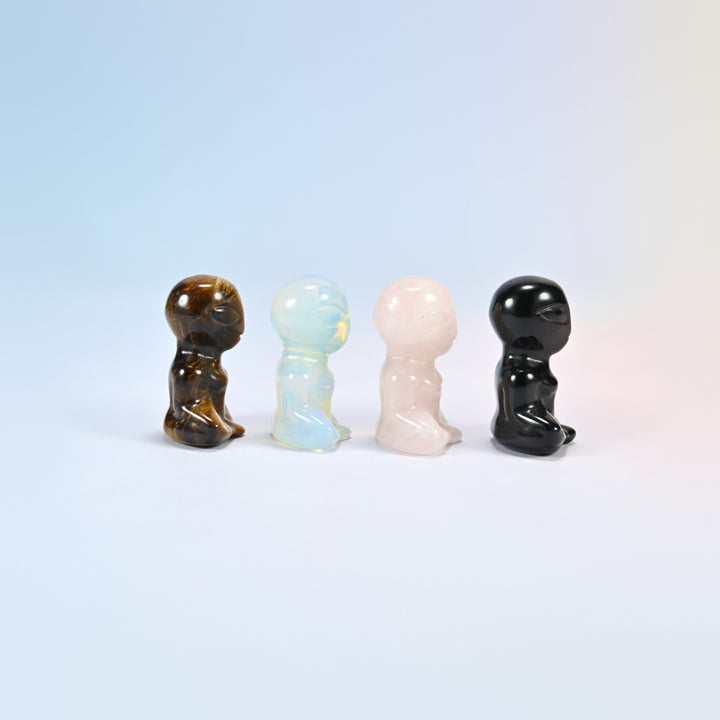 Side view of four meditating alien gemstone figurines showing the big oval heads