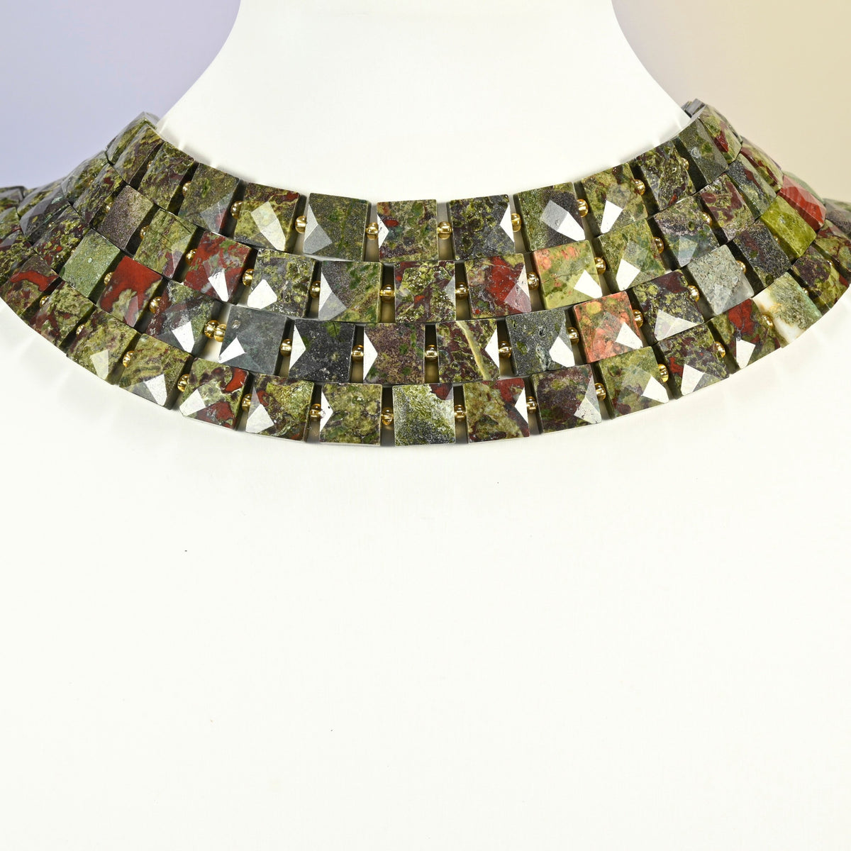 Natural dragon blood stone faceted flat square strands arranged as a layered collar on a white display bust, green and red beads across the neck