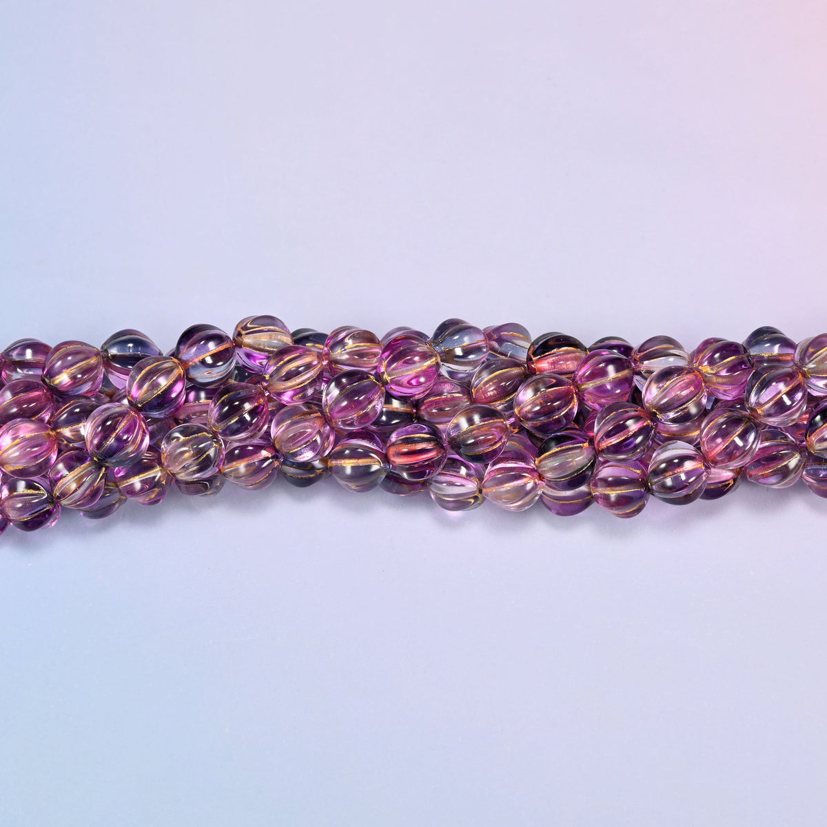 Pink blue gold pumpkin glass beads, 8mm melon rounds, strands laid in a gentle wave straight across the frame.