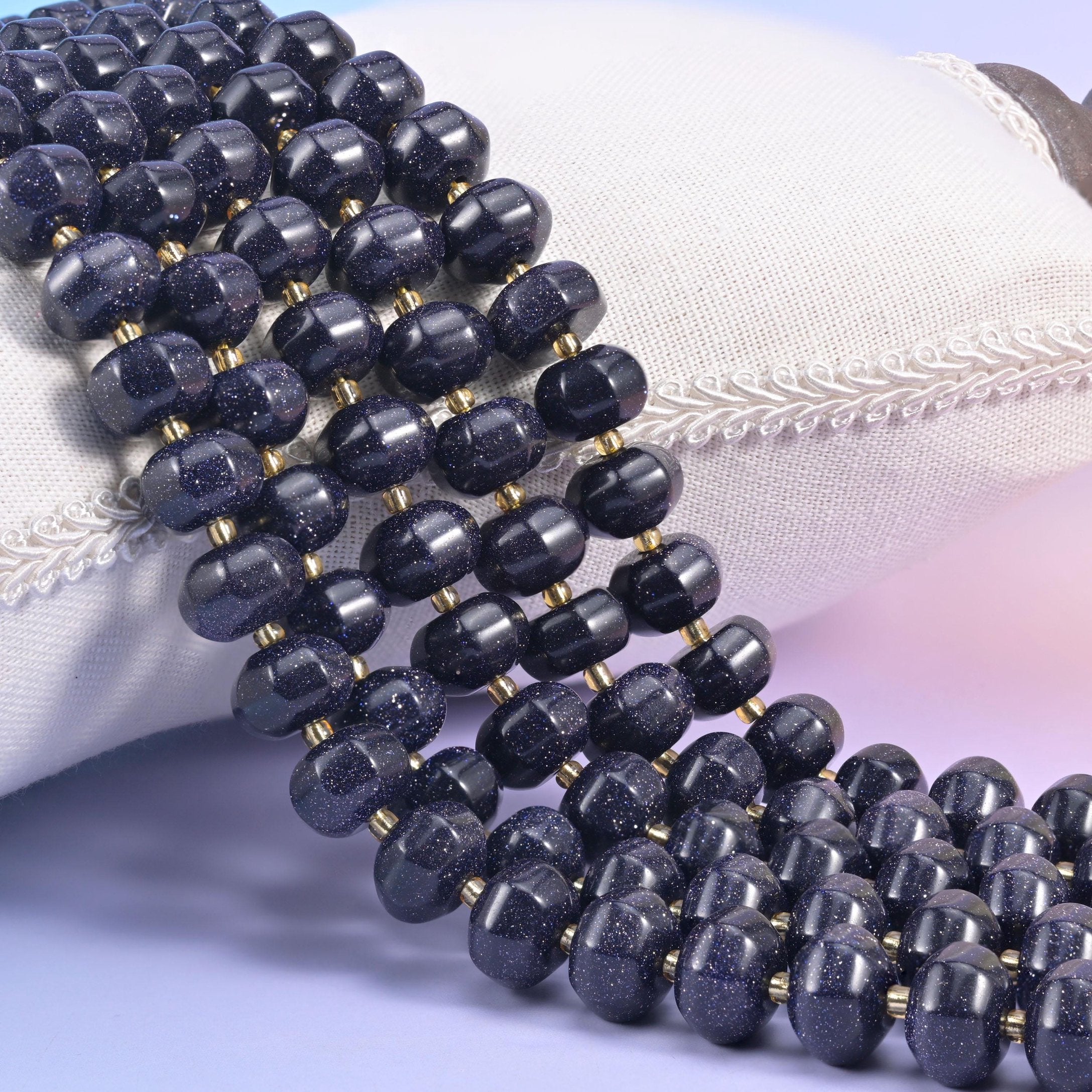 Midnight blue Blue Sandstone pumpkin rondelle strands resting against a white cushion