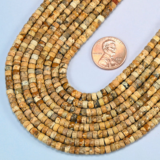 Close view of picture jasper faceted heishi disc strands curving beside a US penny for scale