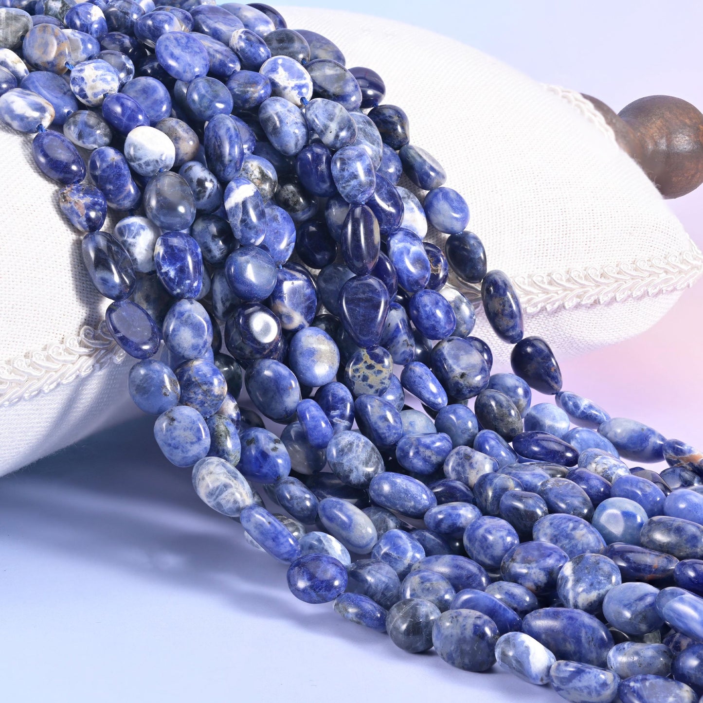 Several strands of blue Sodalite nugget beads piled against a white cushion