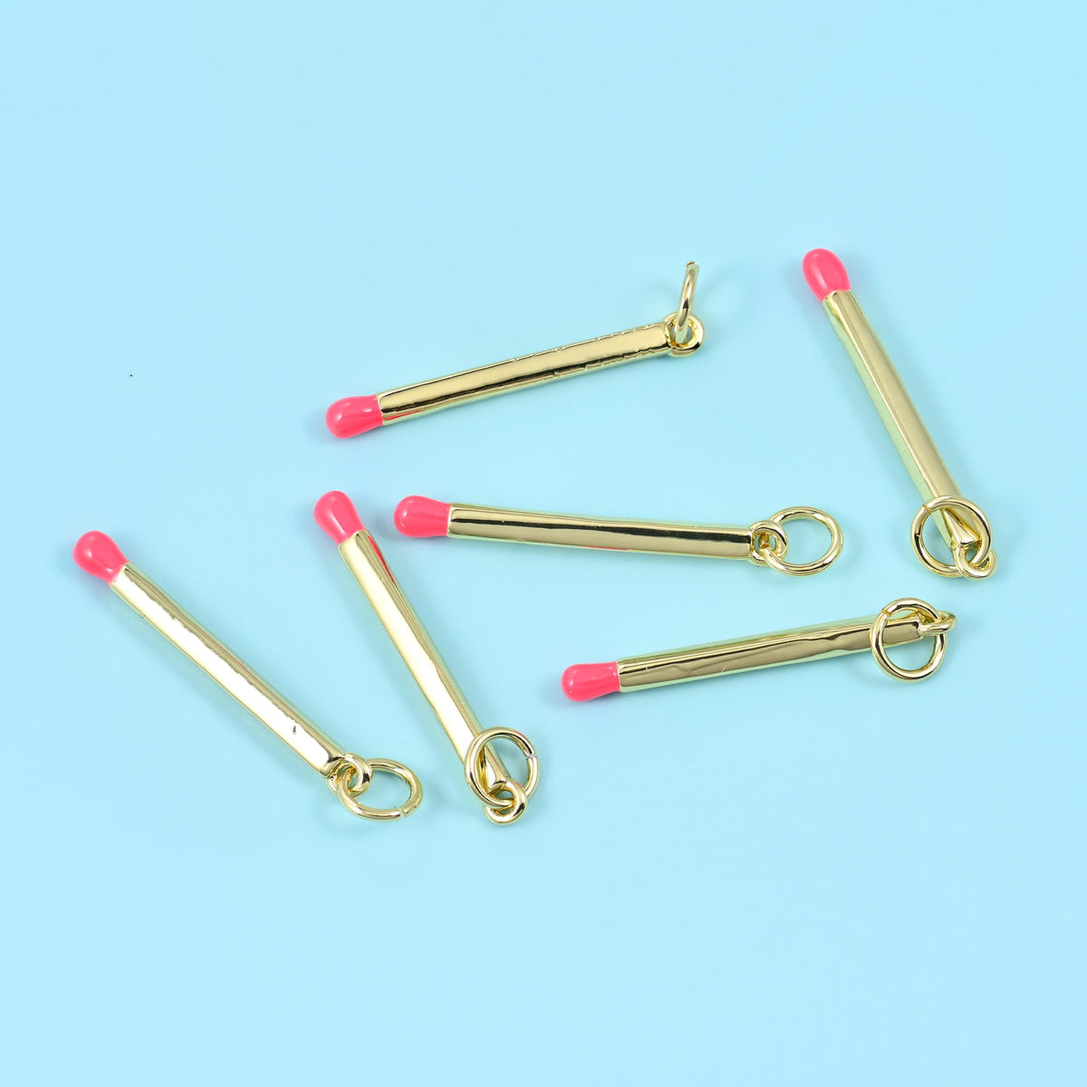 Enamel matchstick pendant in coral pink, six gold bars with coral tips angled across a blue background.