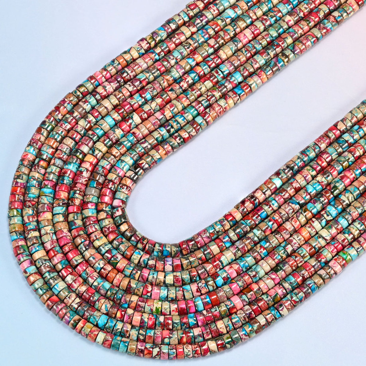 Dyed pink blue sea sediment jasper heishi disc beads 2x4mm in several strands curved into a wide U, raspberry pink, red and turquoise marbled discs