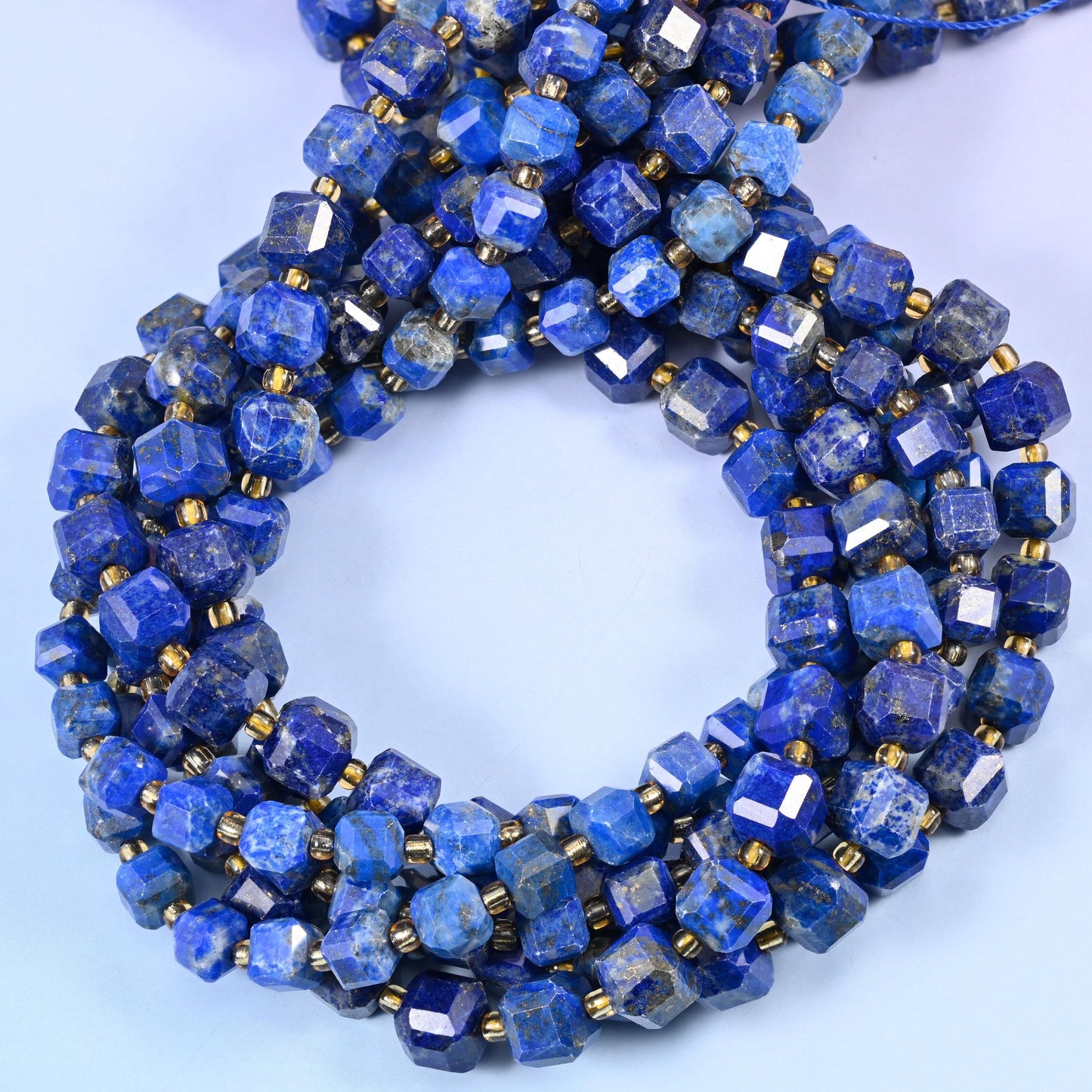 Royal blue cubes streaked with white calcite and grey, lit here and there by tiny gold pyrite flecks, corners cut into facets that spark against the deep colour.